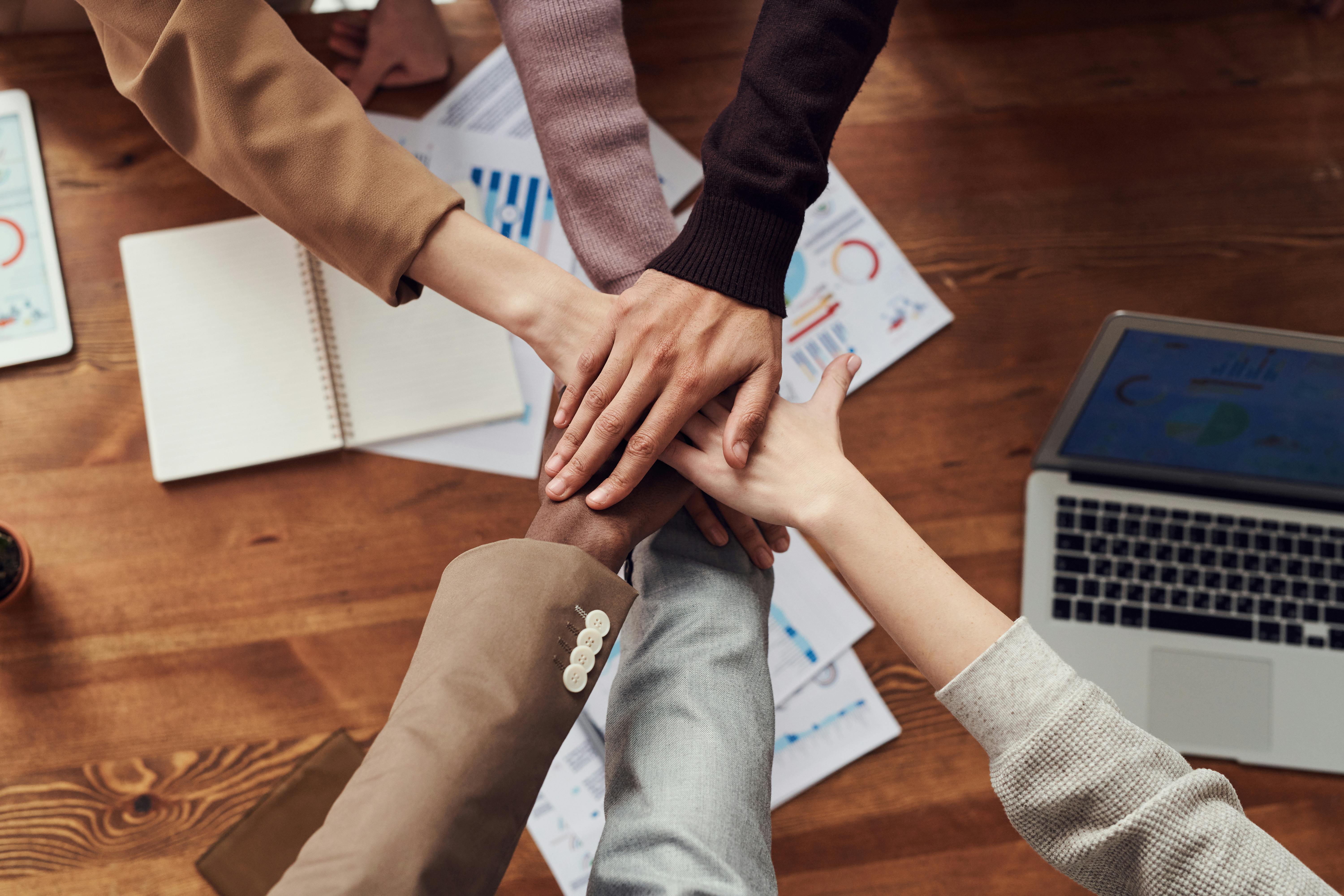 Viele Hände liegen in der Mitte eines Arbeitsplatzes zusammen und formen eine Team-Geste.